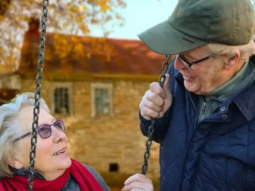 Aktywny seniorzy cieszą się jesiennym dniem na huśtawce. Uśmiechnięta para w otoczeniu złotych liści.