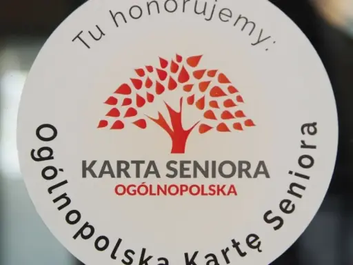 Naklejka z napisem "Tu honorujemy: KARTA SENIORA OGÓLNOPOLSKA" i drzewem. Dostępne zniżki dla posiadaczy ogólnopolskiej karty seniora.