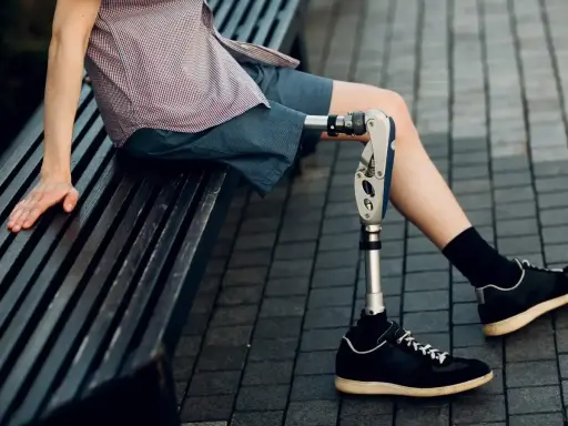 Mężczyzna z nowoczesnymi protezami nóg siedzi na ławce. Jego proteza jest zaawansowana technologicznie.