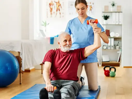 Starszy pan ćwiczy z fizjoterapeutką, podnosząc hantle. To przykład, dla kogo przeznaczony jest bon senioralny – na rehabilitację i aktywność.