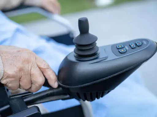 Dłoń starszej osoby na joysticku wózka inwalidzkiego. Czy rozważasz vitafon refundacja NFZ?