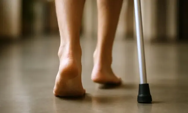 Powolne kroki po złamaniu pięty, wspierane laską. Długotrwała rehabilitacja przynosi efekty.