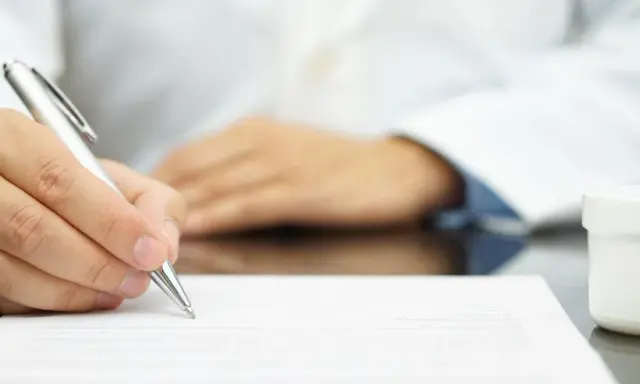 Lekarz pisze receptę farmaceutyczną, obok stoją białe opakowania leków.