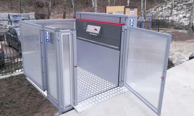 Nowoczesny dźwig dla niepełnosprawnych, z drzwiami otwieranymi na zewnątrz, ułatwia dostęp do budynku.