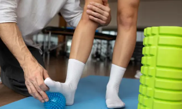 Fizjoterapeuta pomaga pacjentowi z lekkim skręceniem kostki, masując stopę kolczastą piłeczką.