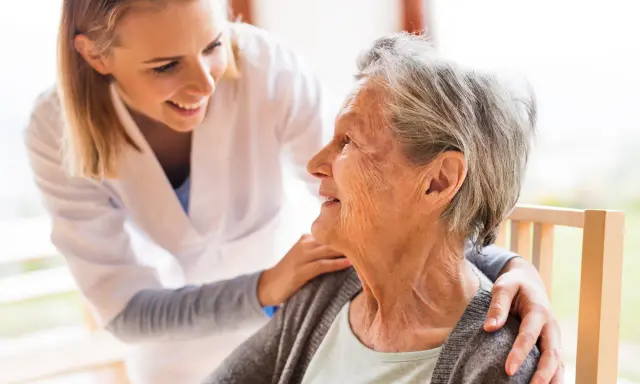 Młoda opiekunka wspiera uśmiechniętą starszą panią, która jest chora na alzheimera.
