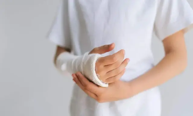 Dziecko z opuchlizną po zdjęciu gipsu nadgarstek, w białej koszulce, z ręką owiniętą bandażem.