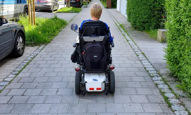 Osoba na wózku elektrycznym porusza się po chodniku. Po udarze, stopień niepełnosprawności może być różny, ale mobilność jest kluczowa.