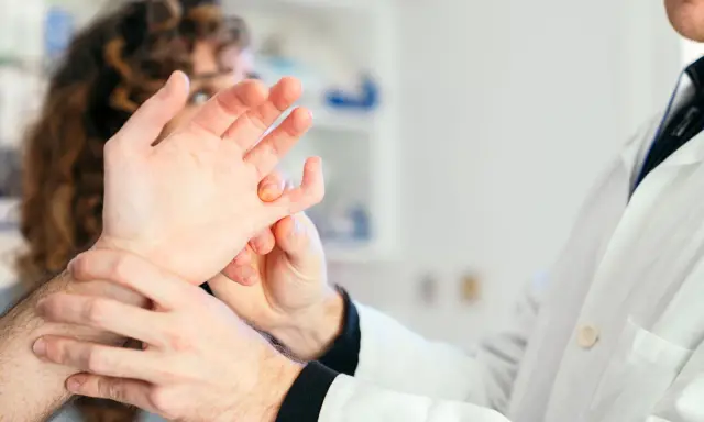 Lekarz bada dłoń pacjenta, który skarży się na bolące stawy.