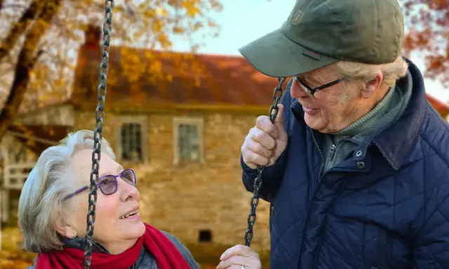 Aktywny seniorzy cieszą się jesiennym dniem na huśtawce. Uśmiechnięta para w otoczeniu złotych liści.