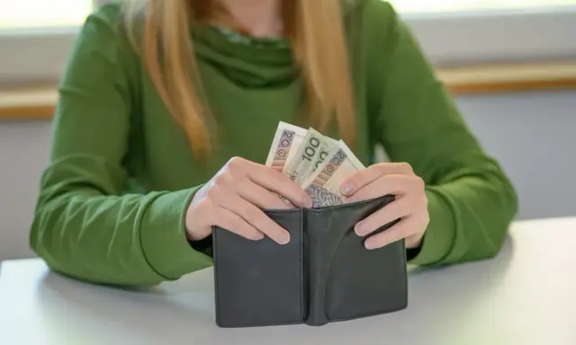 Dłoń wkłada pieniądze do portfela. Może to być wsparcie finansowe dla dziecka z orzeczeniem o niepełnosprawności.