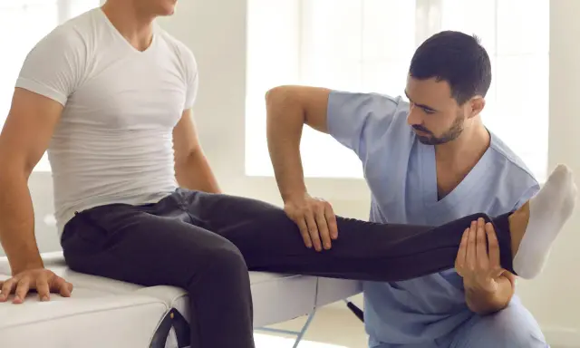 Fizjoterapeuta wykonuje zabiegi rehabilitacyjne, delikatnie unosząc nogę pacjenta.