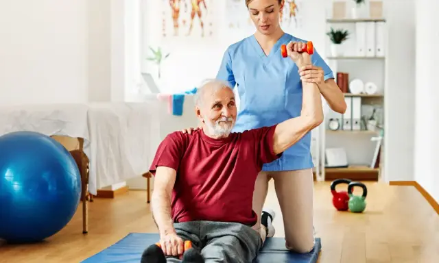 Starszy pan ćwiczy z fizjoterapeutką, podnosząc hantle. To przykład, dla kogo przeznaczony jest bon senioralny – na rehabilitację i aktywność.
