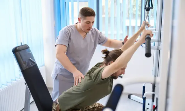 Fizjoterapeuta pomaga pacjentowi w ćwiczeniach na siłowni rehabilitacyjnej. PFRON wspiera takie działania, umożliwiając urlop rehabilitacyjny.