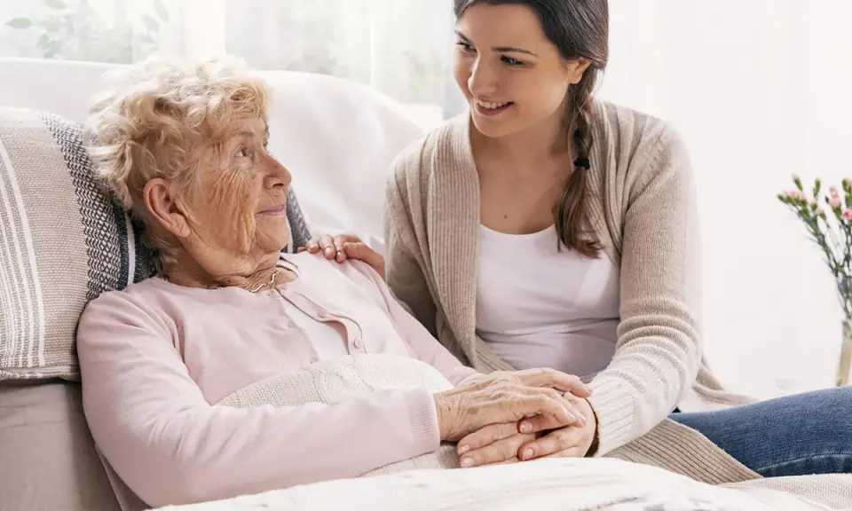 Młoda kobieta wspiera starszą panią, która może potrzebować pomocy w leczeniu alzheimera. Ich dłonie splecione są w geście troski.