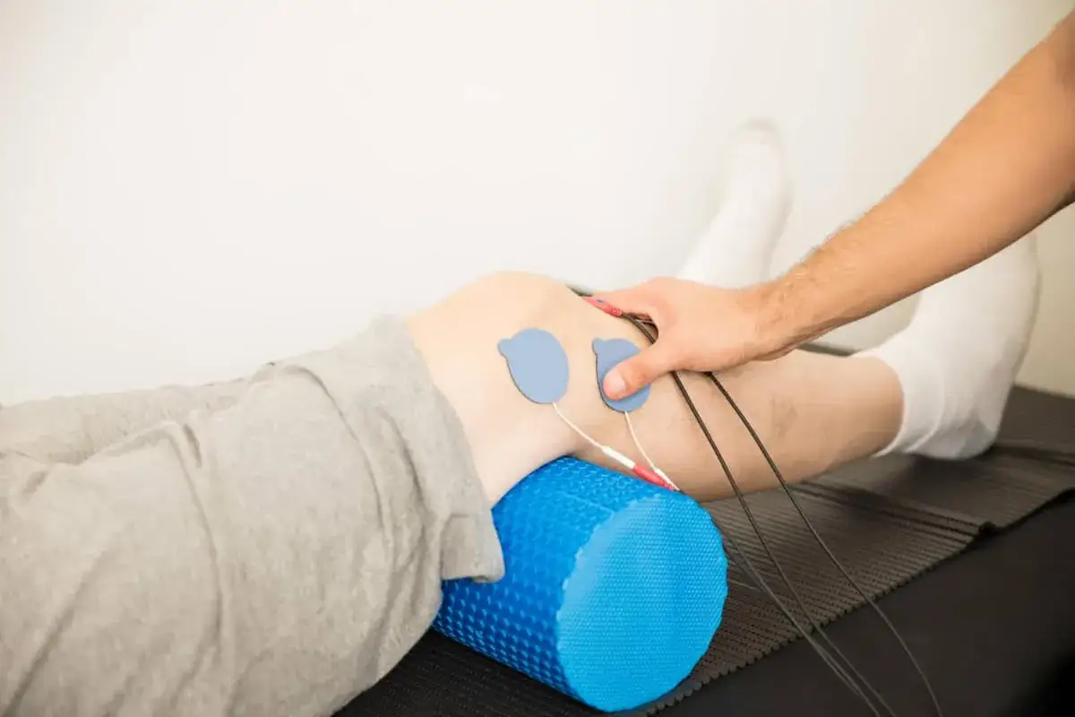 Elektrostymulacja podczas rehabilitacji po operacji łąkotki. Fizjoterapeuta przykłada elektrody do kolana pacjenta, które są podłączone do urządzenia.