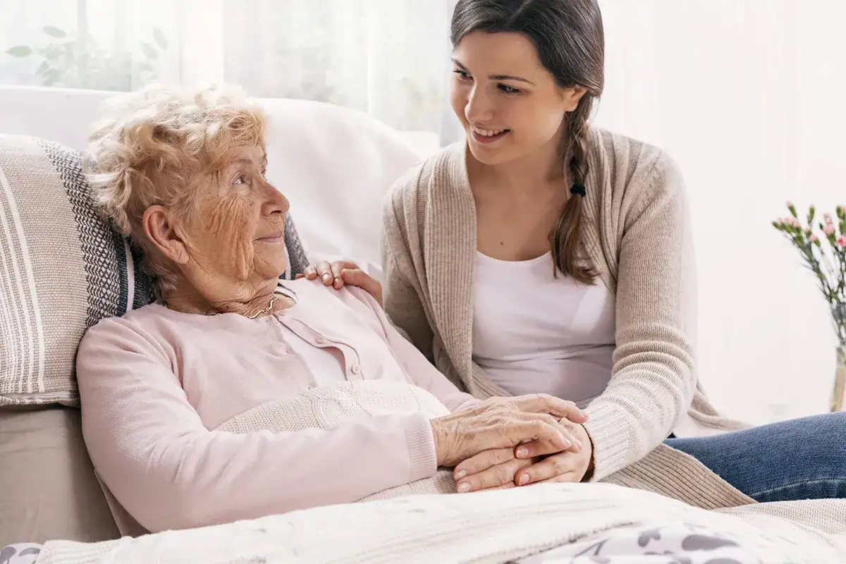 Młoda kobieta wspiera starszą panią, która choruje na alzheimera. Dzielą się chwilą bliskości i zrozumienia.