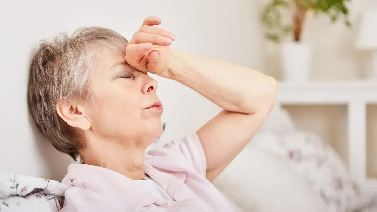 Starsza kobieta z ręką na czole, cierpiąca z powodu zawrotów głowy. Przyczyny zawrotów głowy u osób starszych mogą być różne.