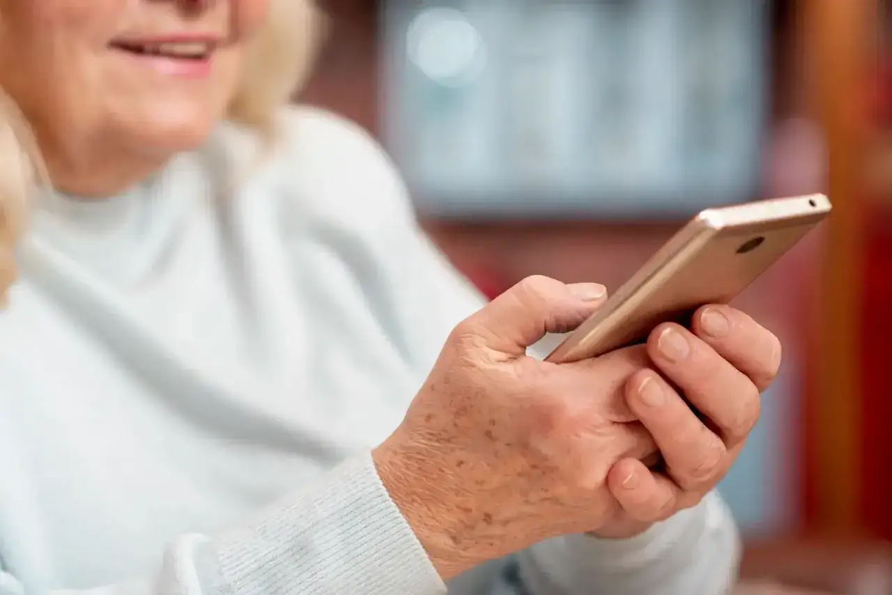 Uśmiechnięta seniorka korzysta z telefonu, odkrywając nowe aplikacje dla seniorów.