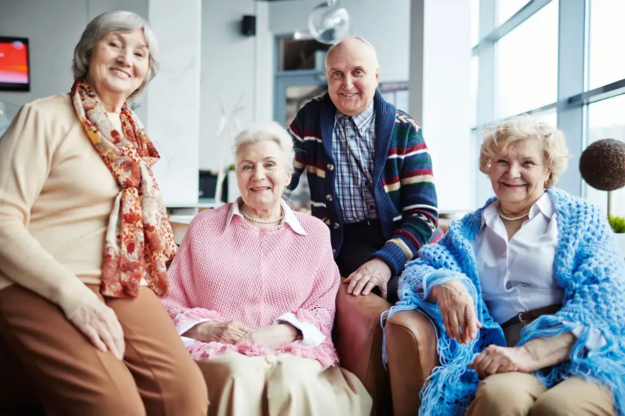 Uśmiechnięci seniorzy siedzą razem w jasnym pomieszczeniu.