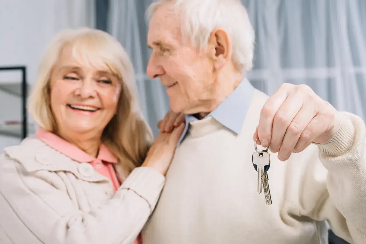 Uśmiechnięta para seniorów, zadowolona z nowego domu. Mężczyzna, jako pacjent geriatryczny, trzyma klucze.