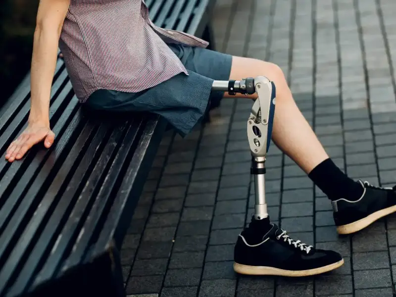 Mężczyzna z nowoczesnymi protezami nóg siedzi na ławce. Jego proteza jest zaawansowana technologicznie.